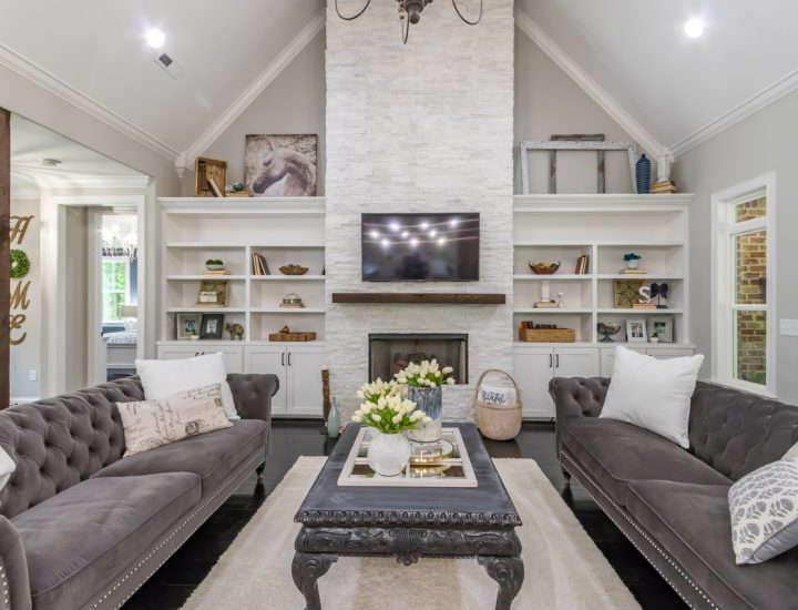Classic living room design with a high vaulted ceiling, white built-in shelving around a stone fireplace, and elegant tufted sofas.