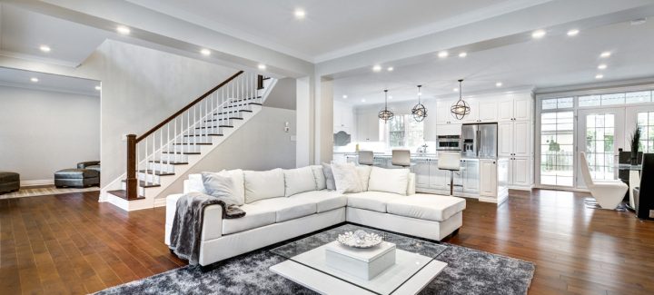 Spacious open concept living room with modern white sectional sofa, stylish chandeliers, and a view of the sleek kitchen, ideal for entertaining.