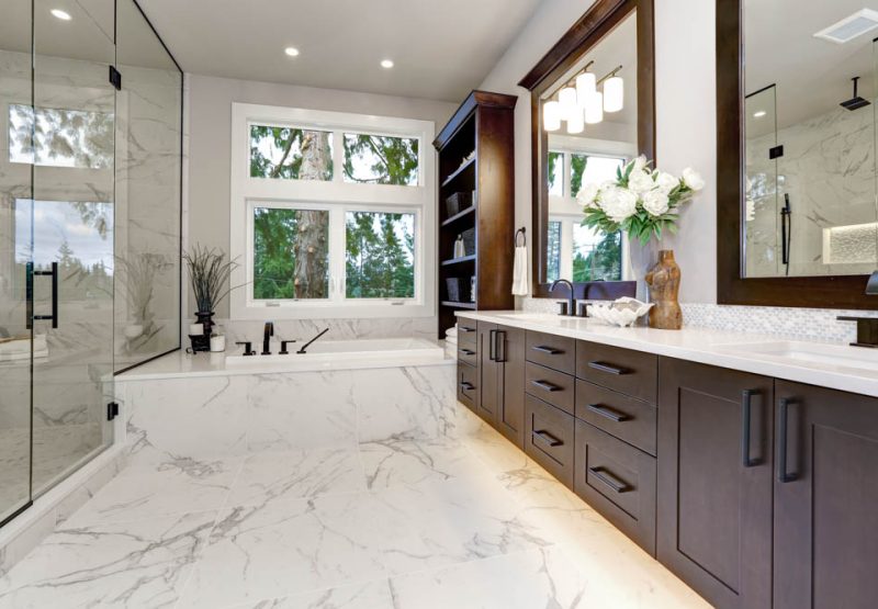 Luxuriously appointed bathroom with marble details, a freestanding bathtub, and a view of the forest through large windows.