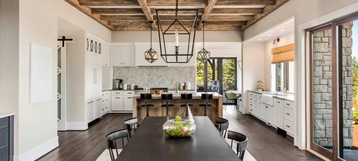 Spacious dining area with a large wooden table, surrounded by a modern kitchen with white cabinetry and exposed wooden beams.