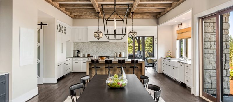 Spacious dining area with a large wooden table, surrounded by a modern kitchen with white cabinetry and exposed wooden beams.